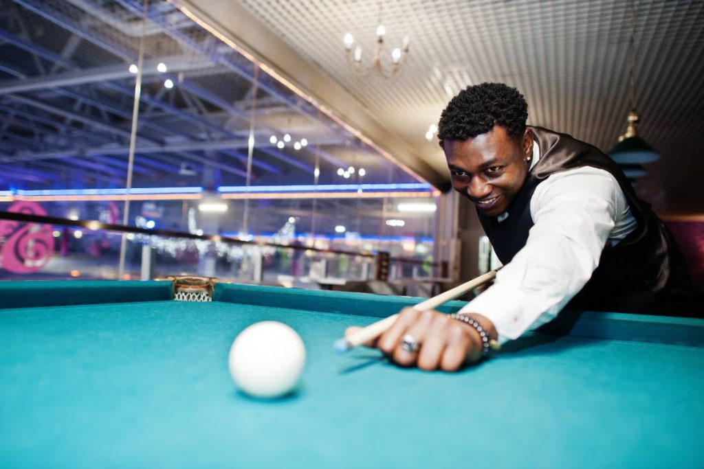 Young handsome african man wearing white shirt, black vest and bow tie play pool billiard.