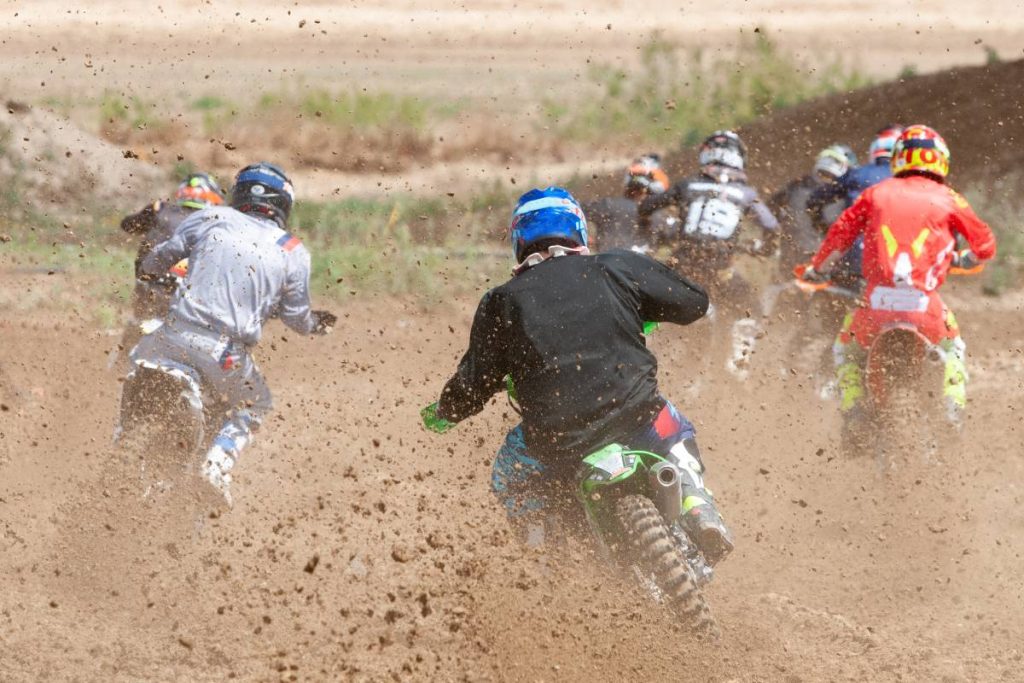 Unrecognized athletes riding a sports motorbike racing fast on a motocross track field. Challenge and competition.