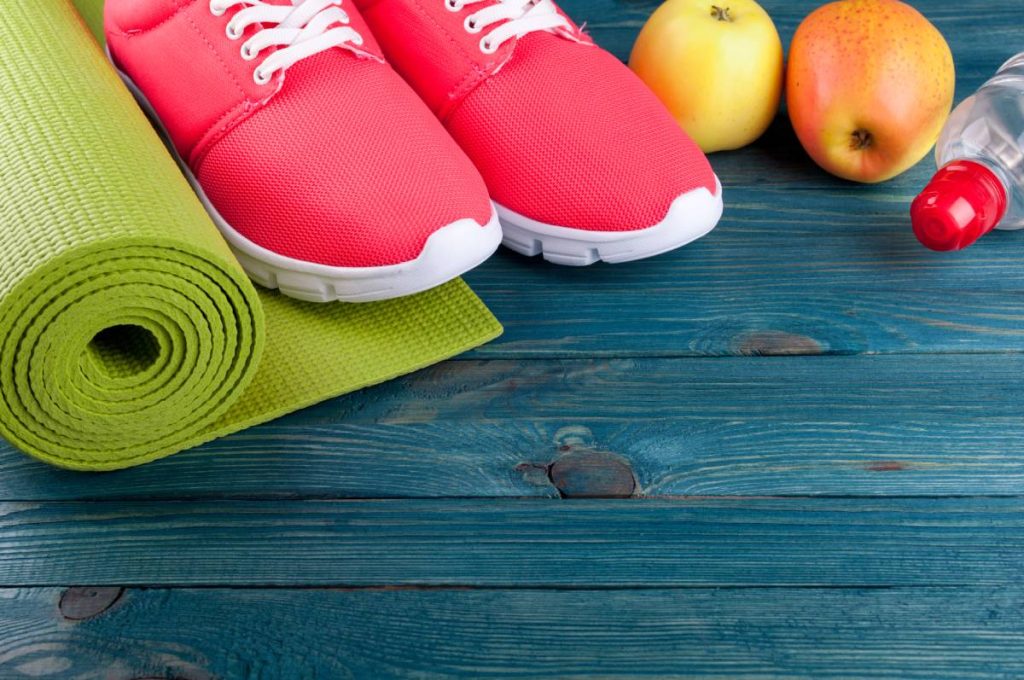 Sport background. Yoga mat, sport shoes, water, apples fruits on wooden background. Healthy lifestyle, diet, yoga, sport concept. Copy space