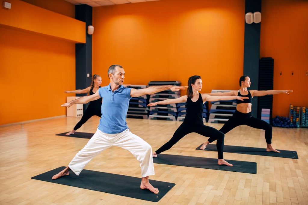 Yoga training class, female group with male trainer in action in gym. Yogi exercise indoor