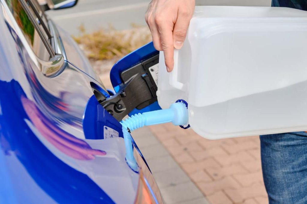 Close up man filling a diesel engine fluid/AdBlue from canister into the tank of blue car. Diesel exhaust fluid for reduction of air pollution. Environmental friendly and eco solution