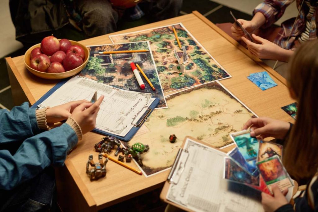 High angle of several youthful kids sitting around table with board game and looking through their cards before one of them making move