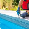 Caucasian Man Building Composite Swimming Pool Deck Inside His Backyard Garden. Drill Driver Close Up.