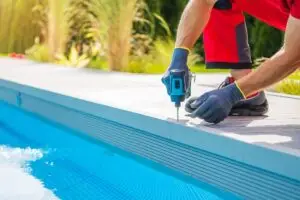Caucasian Man Building Composite Swimming Pool Deck Inside His Backyard Garden. Drill Driver Close Up.