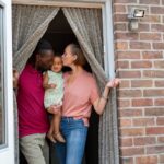 Family with a toddler smiling at each other in a doorway with a brick wall background.