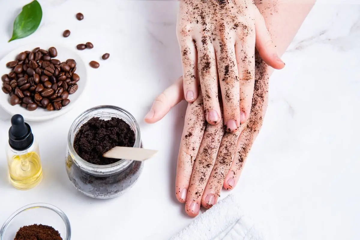 Spa concept. A young woman does a hand massage with a homemade coffee scrub with olive oil on marble background. Top view