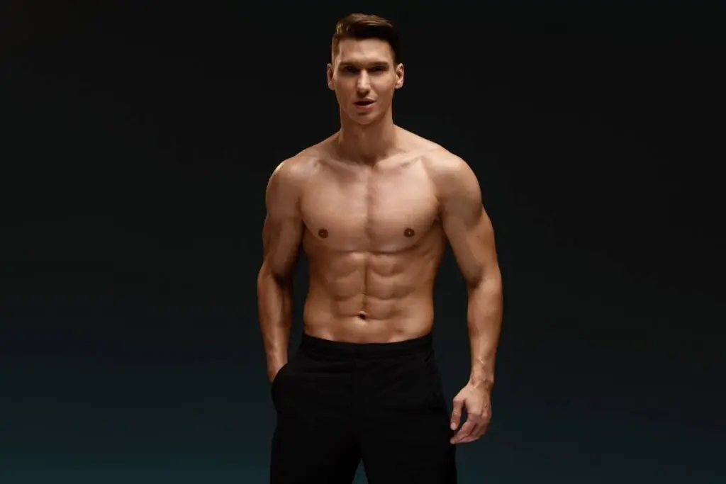 Strong athletic man fitness model posing with naked torso showing six pack abs isolated on blue background. Sport concept