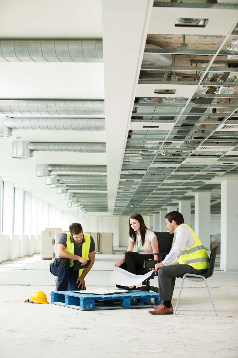 Three people sitting in newly constructed office space, looking at construction plans